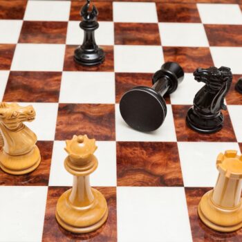 Shown with: 60 cm Da Vinci chess board High-angle view of Staunton Evolution lacquered ebony and boxwood chess pieces with a fallen rook on the 60 cm Da Vinci chess board