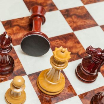 Shown with: 60 cm Da Vinci chess board Overhead view of Staunton Evolution lacquered padauk and boxwood chess pieces with a fallen rook on the 60 cm Da Vinci chess board